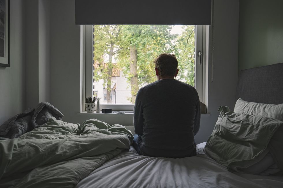 Rear view of an unrecognisable mature man sitting on his bed looking out of the window