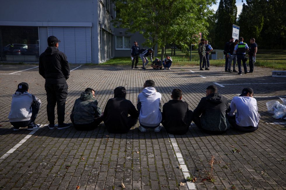 Suspected illegal migrants sit on the ground after they were detained by German police