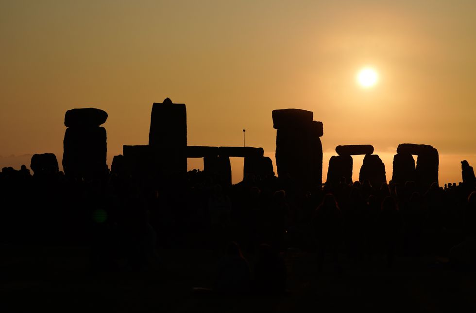 The sun rises behind the stone circle as people gather to take part in the Summer Solstice at Stonehenge in Wiltshire