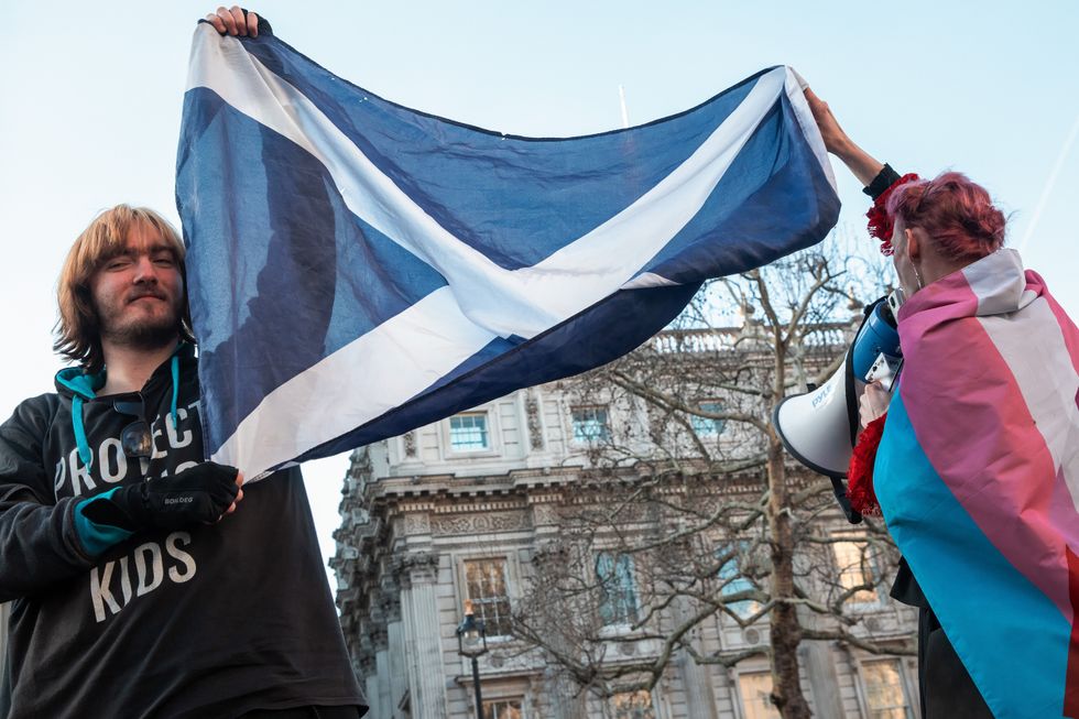 Two people holding a Scottish and trans pride flag