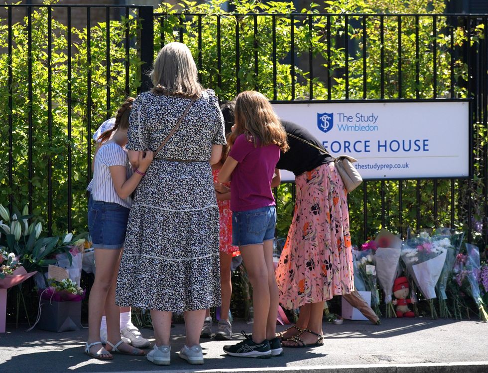 Two women with young girls look at flowers and messages left outside the Study Preparatory School in Wimbledon