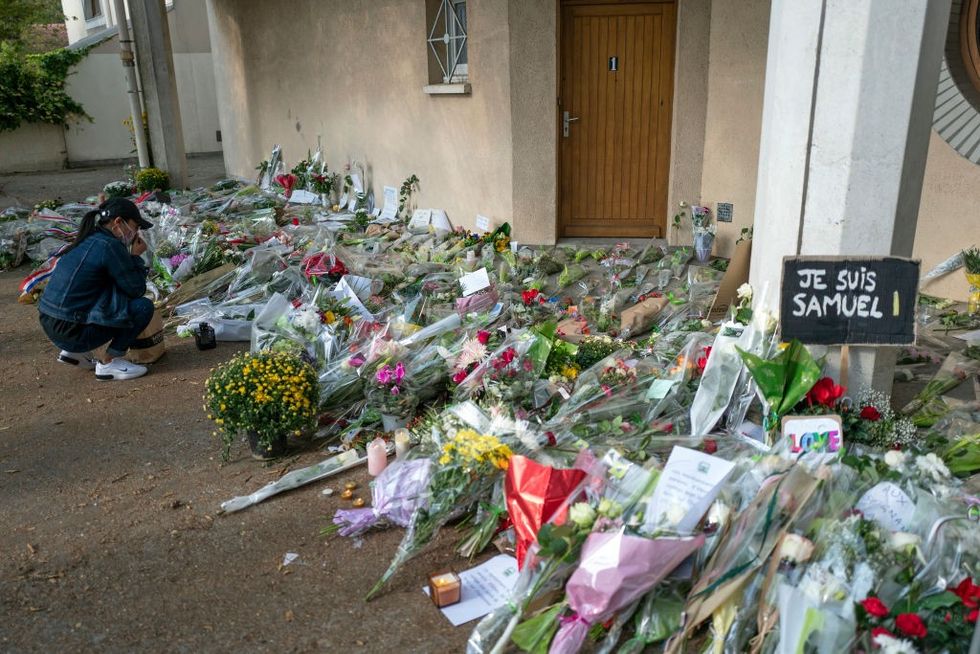 \u200b People gather together and place flowers in front of the middle-school where murdered school teacher Samuel Paty taught on October 18, 2020