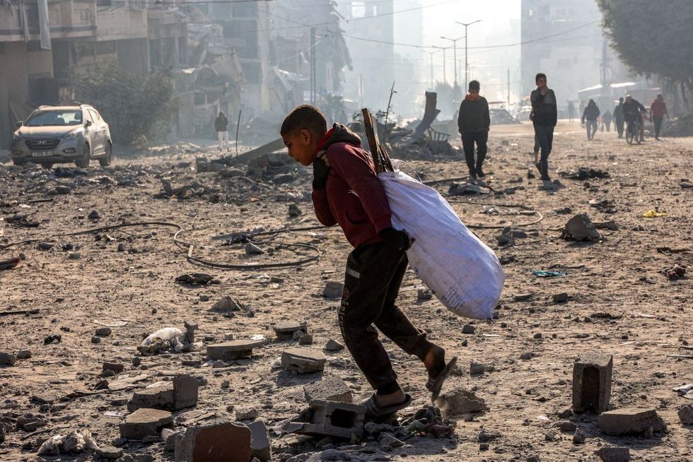 u200bA boy walks with a sack of salvaged items through debris at the site of Israeli bombardment on a residential block in Jalaa Street in Gaza City