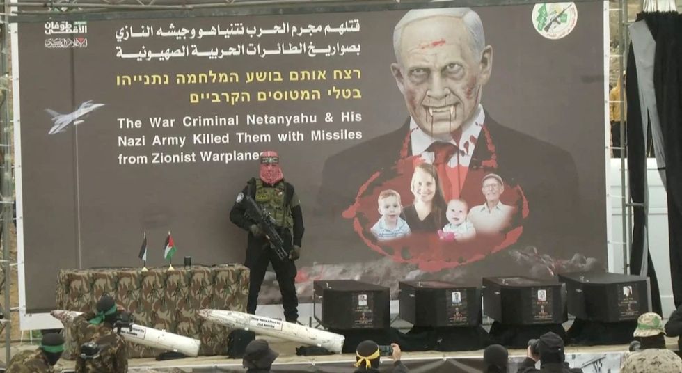 \u200bA Hamas militant stands near coffins during the handover of deceased hostages Oded Lifschitz, Shiri Bibas and her two children Kfir and Ariel Bibas