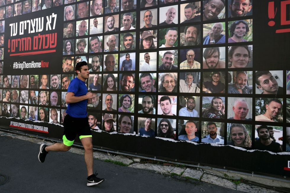 \u200bA man runs past a billboard featuring portraits of Israelis hostages held in the Gaza Strip