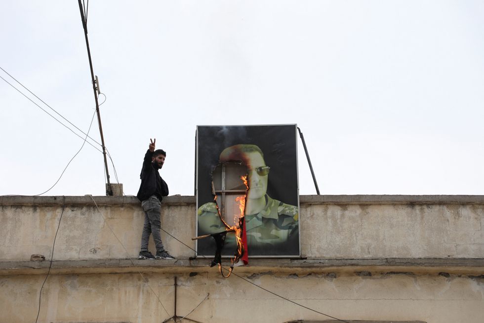 u200bA person gestures next to a burning picture of President Bashar al-Assad, after rebels seized the capital and ousted the president