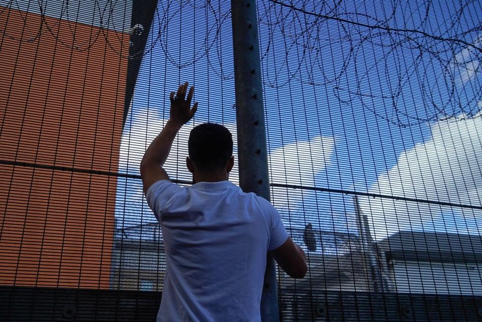 u200bA protester communicates with those inside at the perimeter fence of Brook House immigration removal centre beside Gatwick Airport