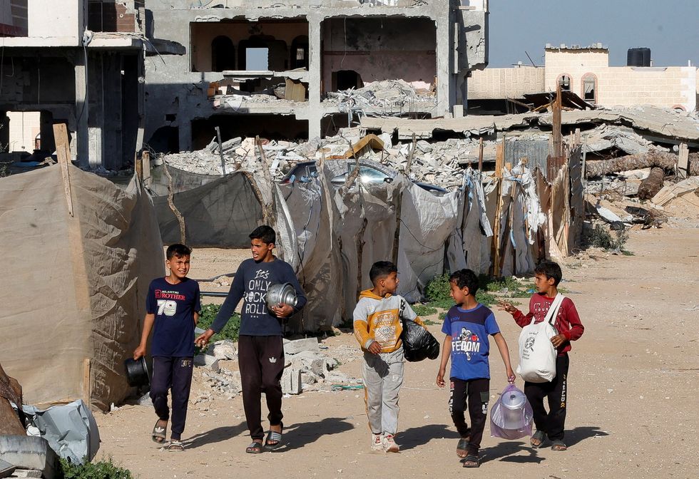 \u200bPalestinian children walk with containers to receive food cooked by a charity kitchen