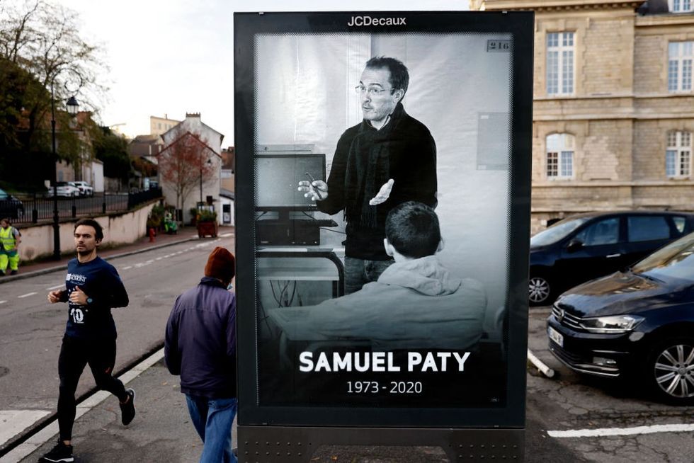 \u200bPedestrians pass by a poster depicting French teacher Samuel Paty placed in the city center of Conflans-Sainte-Honorine