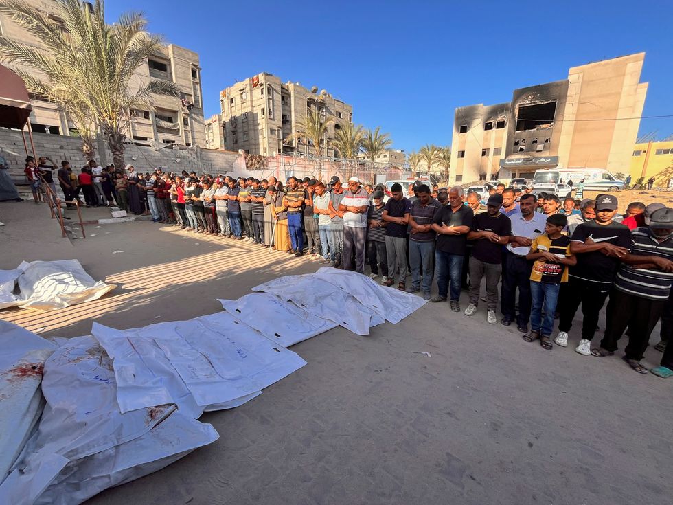 \u200bPeople pray next to the bodies of Palestinians killed in Israeli strikes, amid the Israel-Hamas conflict, in Khan Younis