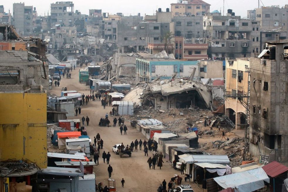 \u200bPeople walk past stalls selling goods amid the rubble of buildings destroyed during previous Israeli strikes, in Khan Yunis in the southern Gaza Strip