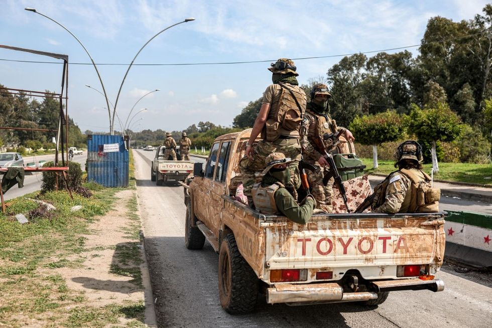 \u200bSecurity forces loyal to the interim Syrian government ride in the back of a vehicle moving along a road in Syria's western city of Latakia