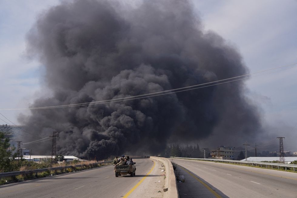 \u200bSmoke rises while members of the Syrian forces ride on a vehicle as they battle against a nascent insurgency