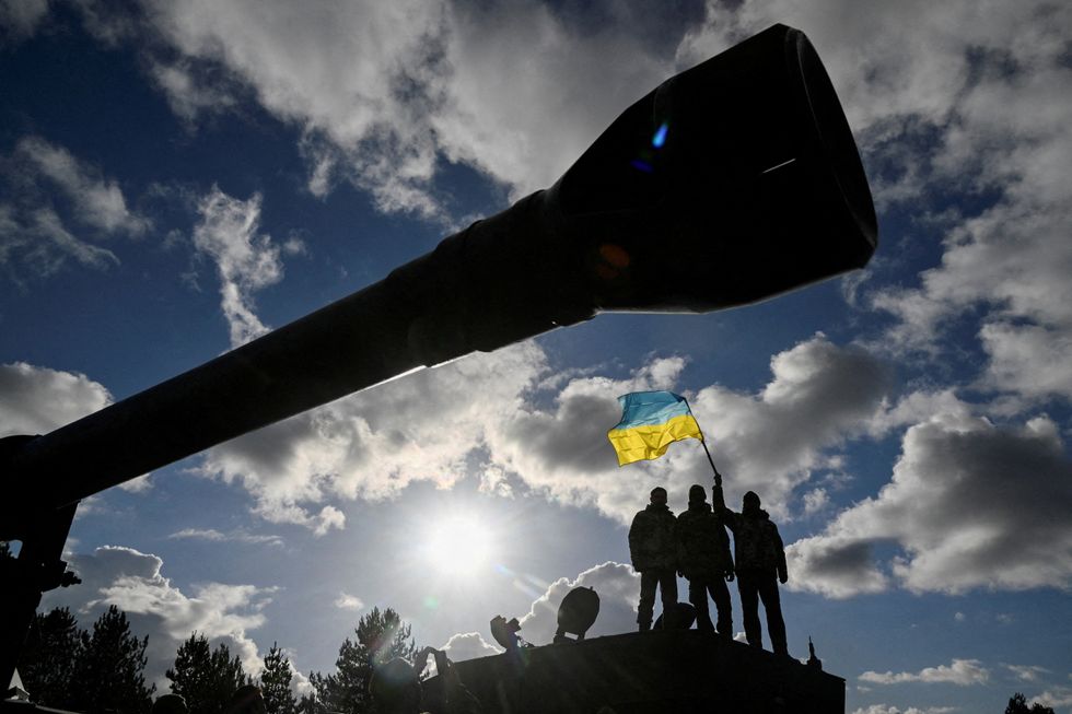 Ukrainian personnel hold a Ukrainian flag as they stand on a Challenger 2 tank during training at Bovington Camp, near Wool