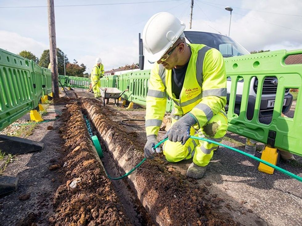 virgin media engineer in uniform pulling out a fibre-optic cable from the ground 