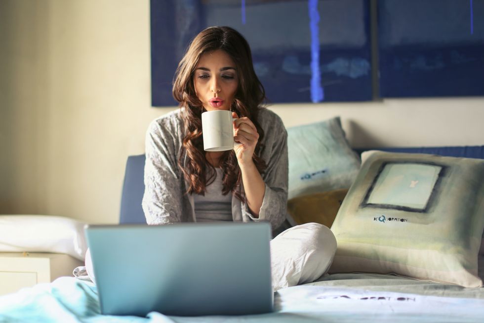 Woman drinking coffee while working on her bed