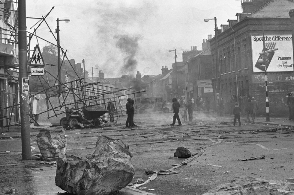 Young Belfast men gather around burning vehicles in a debris-strewn Belfast street. The fires were set as a harassment tactic against the British soldiers stationed in Belfast to restore order.