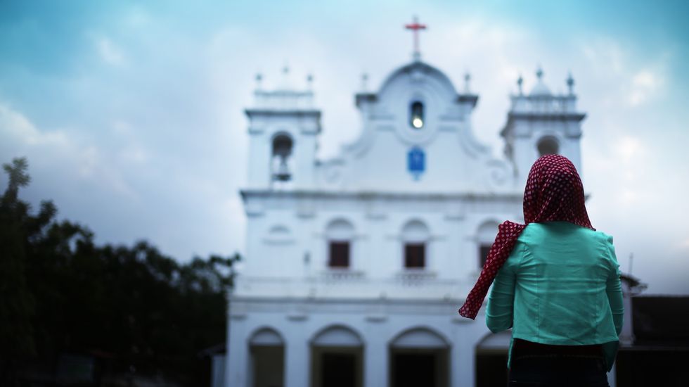 Young Christian woman standing in front of holy church and she praying to God, Goa/Indi